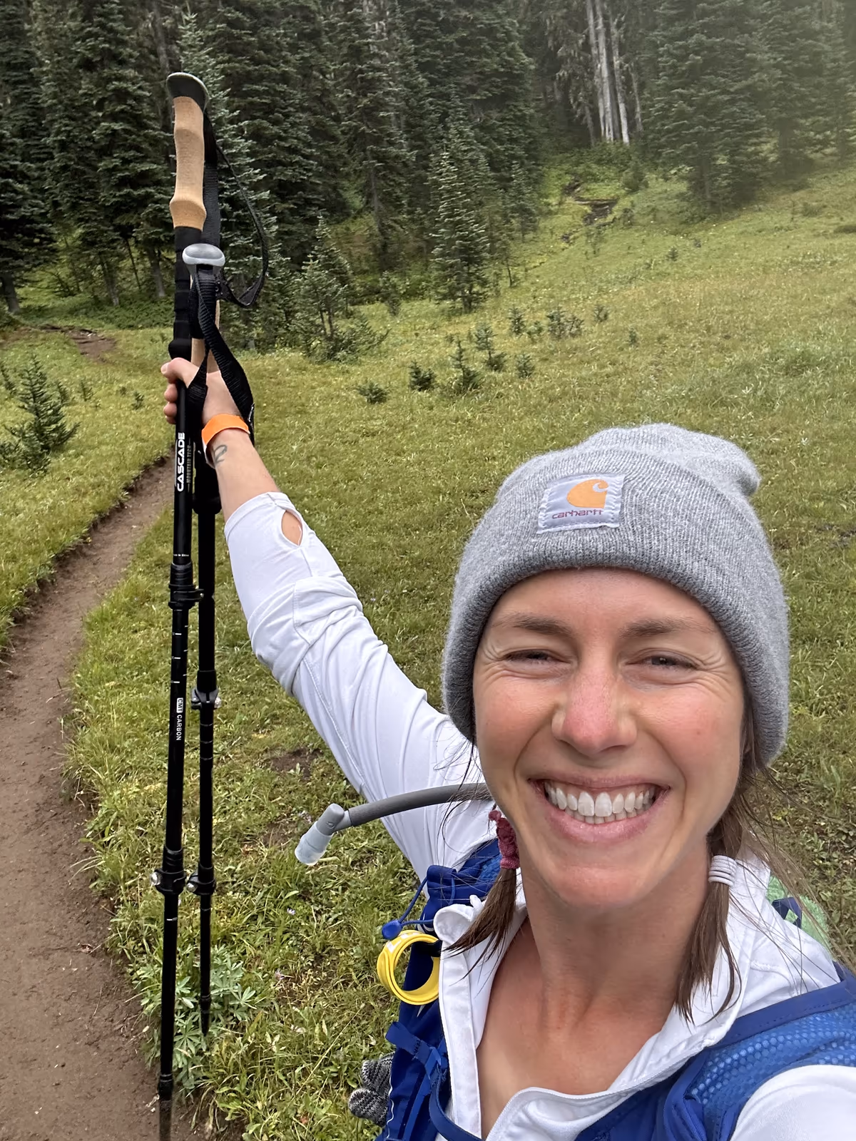 Lizi Shaw smiling on a mountain trail and holding up her hiking poles